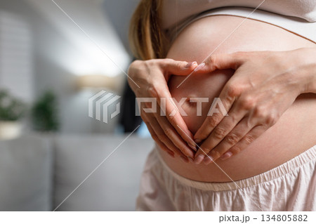 Woman's hands forming heart shape on pregnant belly, symbolizing love and anticipation for new life 134805882
