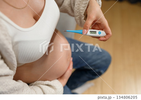Pregnant woman holding digital thermometer showing normal temperature, focusing on belly and health monitoring Pregnant woman holding digital thermometer showing normal temperature, focusing on belly and health monitoring 134806205