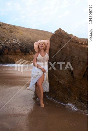 Smiling woman leaning on rock by seaside on sandy Smiling woman leaning on rock by seaside on sandy 134806719