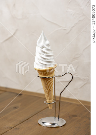 木目テーブルに置かれたバニラソフトクリームコーンと金属スタンド 134809072