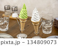 木製テーブルのカフェに並ぶ抹茶ソフトクリームとバニラソフトクリームコーン 134809073