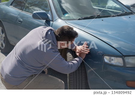 A Caucasian man tries to repair damage to a car body with his hands. A Caucasian man tries to repair damage to a car body with his hands. 134809492