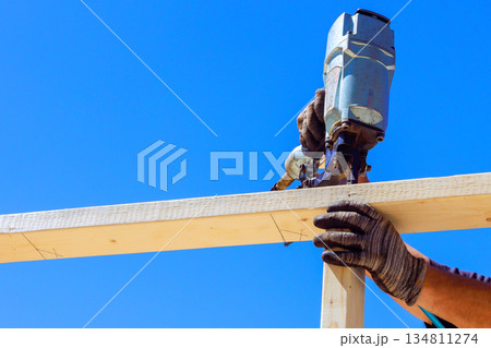 Worker holds wood in place while using pneumatic nail gun to build beams frame. Worker holds wood in place while using pneumatic nail gun to build beams frame. 134811274