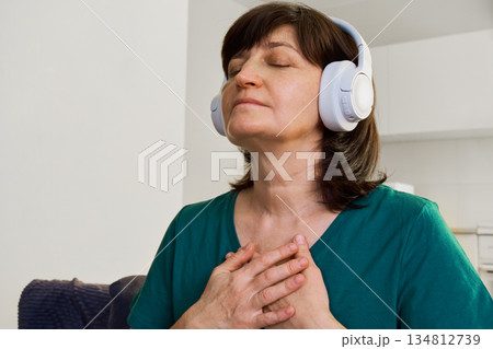 Woman wearing headphones with eyes closed embracing self-care and mindfulness at home 134812739