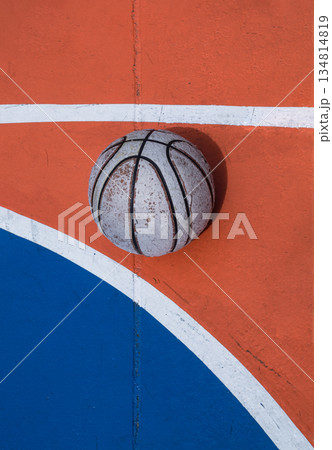 A weathered basketball sits in stark contrast against the vibrant orange and blue expanse of the court, defined by crisp white lines. A weathered basketball sits in stark contrast against the vibrant orange and blue expanse of the court, defined by crisp white lines. 134814819