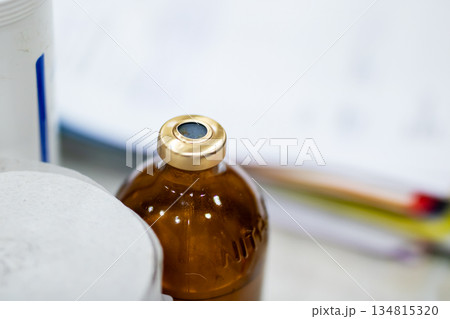 Vaccine bottle focus, Detailed shot showing vaccine vial with metal seal on laboratory bench Vaccine bottle focus, Detailed shot showing vaccine vial with metal seal on laboratory bench 134815320