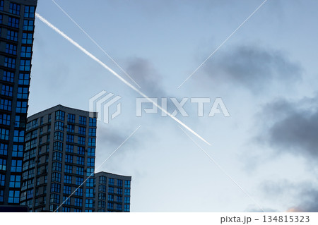 Cityscape with flying jet trail, Dusk city skyline showing airplane streaks and silhouettes 134815323