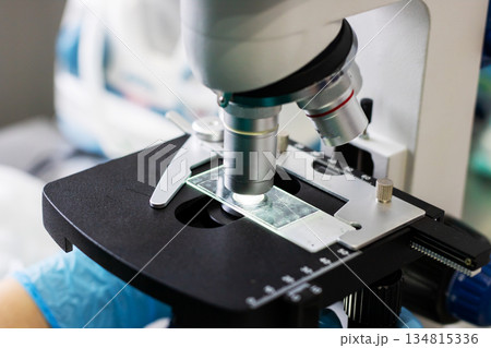 Clinical scientist analyzing cellular features using microscope on prepared glass slide 134815336