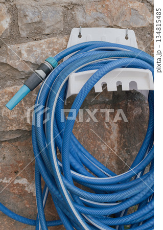 Garden hose coiled on wall mounted holder by stone wall Garden hose coiled on wall mounted holder by stone wall 134815485