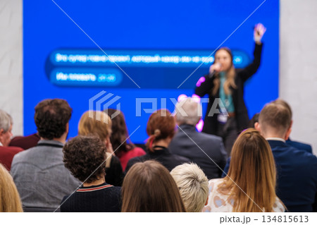 Speaker presents at conference to engaged audience under bright blue screen during live seminar 134815613