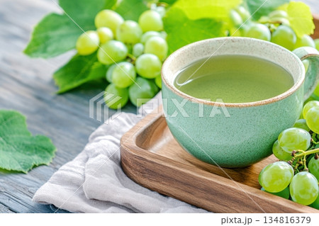 Cozy morning setting with a sage green ceramic cup of herbal tea, fresh green grapes, and a linen napkin on a wooden tray Cozy morning setting with a sage green ceramic cup of herbal tea, fresh green grapes, and a linen napkin on a wooden tray 134816379