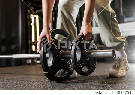Close up of female athlete adding weight plates to barbell for strength workout in modern fitness gym Close up of female athlete adding weight plates to barbell for strength workout in modern fitness gym 134819251