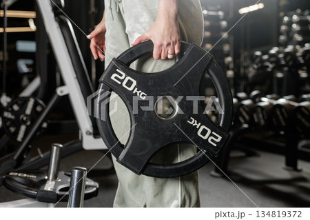 Close up of female athlete holding weight plate in fitness club while setting up equipment for strength workout 134819372
