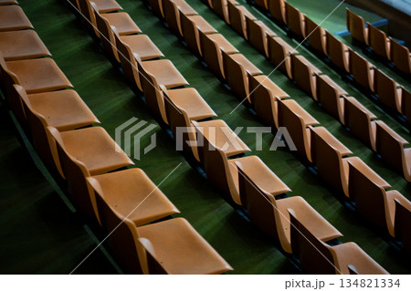 Orange stadium seats with green flooring. Combination of orange and green. Empty stands during competitions. No one in stadium seats. Watching sports Orange stadium seats with green flooring. Combination of orange and green. Empty stands during competitions. No one in stadium seats. Watching sports 134821334