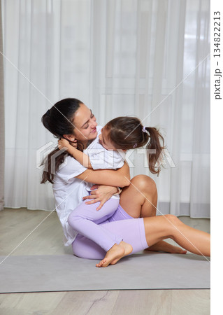 Happy mother hugging smiling daughter during home fitness on a yoga mat Happy mother hugging smiling daughter during home fitness on a yoga mat 134822213
