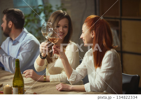 Women clinking wine glasses sitting at dinner table with candles and food. 134822334