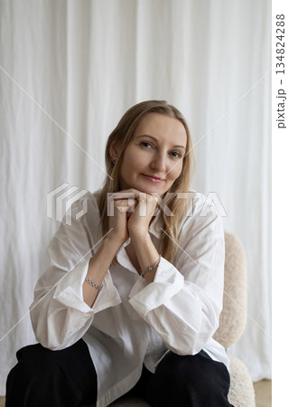 Portrait of smiling woman in white shirt sitting in minimalist interior Portrait of smiling woman in white shirt sitting in minimalist interior 134824288