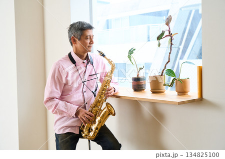 サックスを持って窓辺に佇む男性 134825100