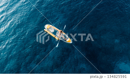 Woman swims on kayak in summer blue sea. Drone view, top down Woman swims on kayak in summer blue sea. Drone view, top down 134825591