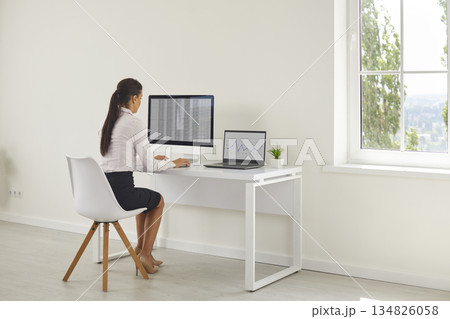 Female analyst reviewing spreadsheets at desktop with laptop financial graphs Female analyst reviewing spreadsheets at desktop with laptop financial graphs 134826058