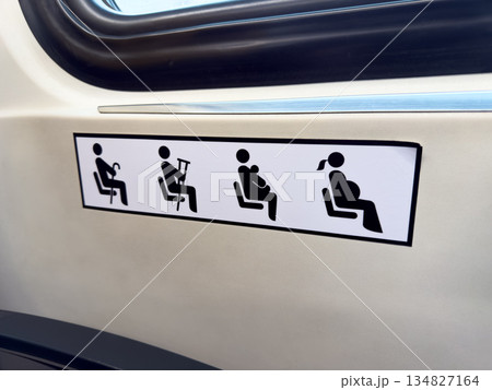 Black signs on white sticker next to seat on public vehicle indicate seats for people with difficulty standing. Give up your seat to elderly person, pregnant woman, or passenger with child 134827164