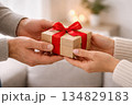 Close-up stock photo of hands giving a small wrapped Valentine's Day gift with red ribbon 134829183
