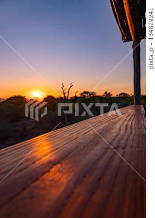 Sunset over a natural landscape with a wooden railing in the foreground Sunset over a natural landscape with a wooden railing in the foreground 134829241