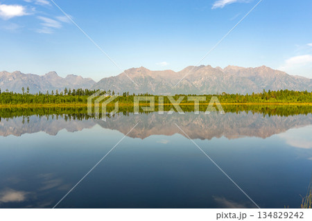Clear reflection of green forest and rugged mountains on calm lake surface 134829242