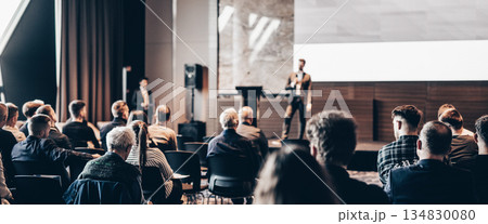 Speaker giving a talk in conference hall at business event. Rear view of unrecognizable people in audience at the conference hall. Business and entrepreneurship concept 134830080