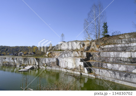 Huge geometric stone shapes and autumn birches reflected in the water of the abandoned marble quarry Huge geometric stone shapes and autumn birches reflected in the water of the abandoned marble quarry 134830702