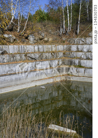 Huge geometric stone shapes and autumn birches reflected in the water of the abandoned marble quarry Huge geometric stone shapes and autumn birches reflected in the water of the abandoned marble quarry 134830703