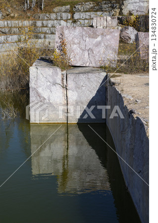 Huge cubic and geometric stone shapes are reflected in the water of the abandoned marble quarry Huge cubic and geometric stone shapes are reflected in the water of the abandoned marble quarry 134830724