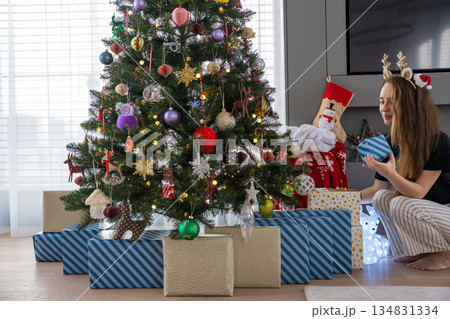 Woman placing wrapped gifts under decorated Christmas tree with colorful ornaments. 134831334