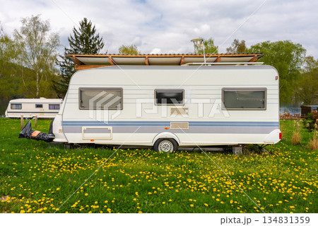 Two retro camper trailers parked on green grass near lake with wooden shelter, blooming dandelion 134831359
