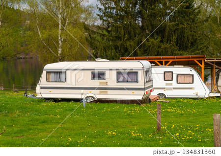 Two retro camper trailers parked on green grass near lake with wooden shelter and blooming dandelion 134831360