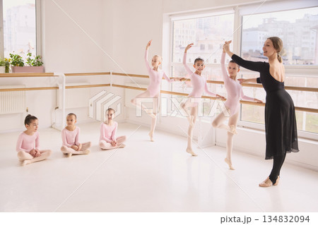 Ballet teacher guiding young girls during classical dance class at barre. 134832094
