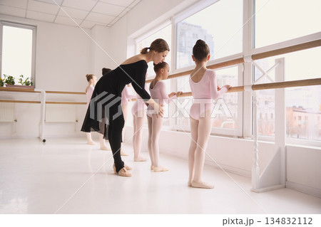 Ballet teacher correcting posture of young girls at barre in dance studio 134832112