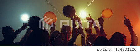Party crowd holding balloons under festive stage lights. Banner 134832120