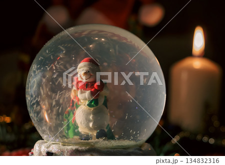 Snow Globe with Snowman and Christmas Tree in Warm Candlelit Holiday Setting Snow Globe with Snowman and Christmas Tree in Warm Candlelit Holiday Setting 134832316