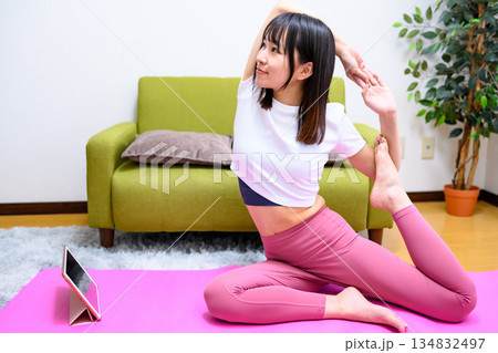 鳩のポーズ　タブレットでYouTube動画を見ながら自宅で柔軟、ヨガをする若い女性　ヨガウェア 134832497