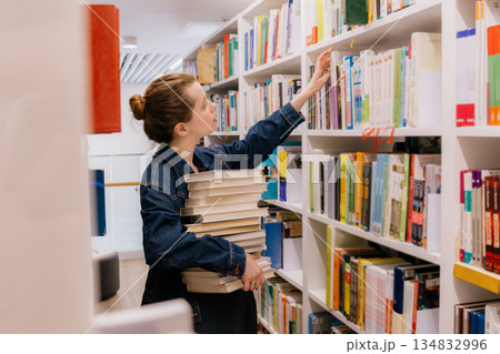 woman is sitting at shelves in library, student is choosing book. library is filled with books. 134832996