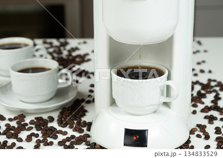 Close-up of fresh hot coffee dripping from a white machine into a cup. 134833529