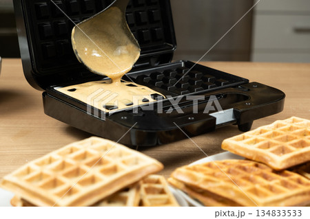 Close-up of Homemade Dough Being Added to a Waffle Iron for Baking. Close-up of Homemade Dough Being Added to a Waffle Iron for Baking. 134833533