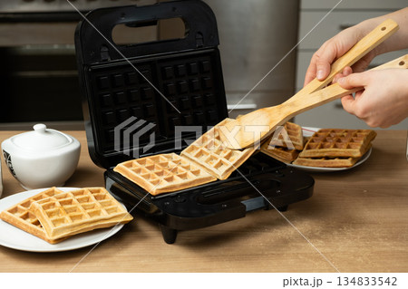 Taking Out Hot Golden-Brown Waffles from an Electric Maker in a Home Kitchen. Taking Out Hot Golden-Brown Waffles from an Electric Maker in a Home Kitchen. 134833542