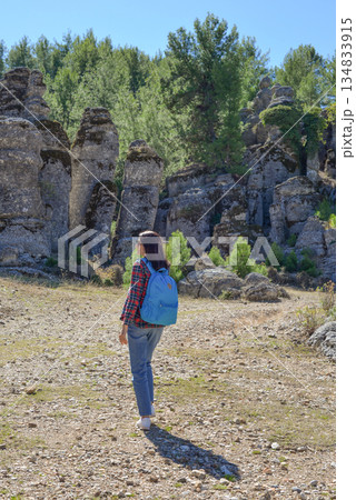 A woman tourist with a backpack on her back walks through the ancient city of Selga, admiring the wonderful nature and wonderful rocks. Turkey, Antalya. A woman tourist with a backpack on her back walks through the ancient city of Selga, admiring the wonderful nature and wonderful rocks. Turkey, Antalya. 134833915