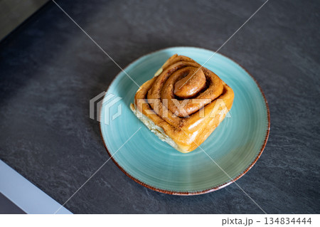 Classic cinnamon roll on an artisan ceramic plate in a home kitchen, top view. Warm tones and natural light create an inviting feel. Concept of breakfast, pastry, comfort, homemade. 134834444