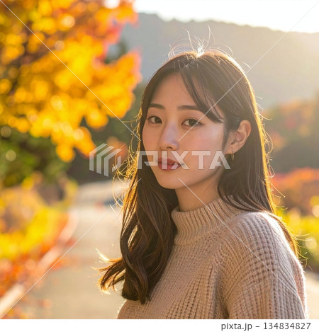 柔らかな夕陽に照らされた秋の風景の中で、落ち着いた表情を見せる女性の場面 134834827