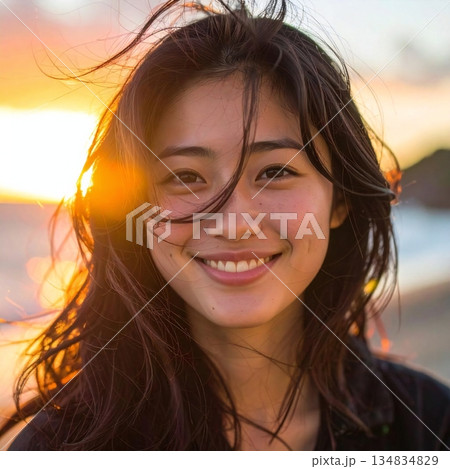 夕陽のきらめきと風に揺れる髪が重なり、自然な笑顔が心地よい温かさを感じさせる美しい場面 134834829