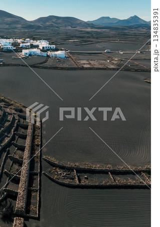 White buildings, town among volcanic black mountains and lava formations in Lanzarote, Canary Islands. 134835391