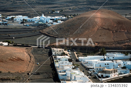 White buildings, town among volcanic black mountains and lava formations in Lanzarote, Canary Islands. 134835392